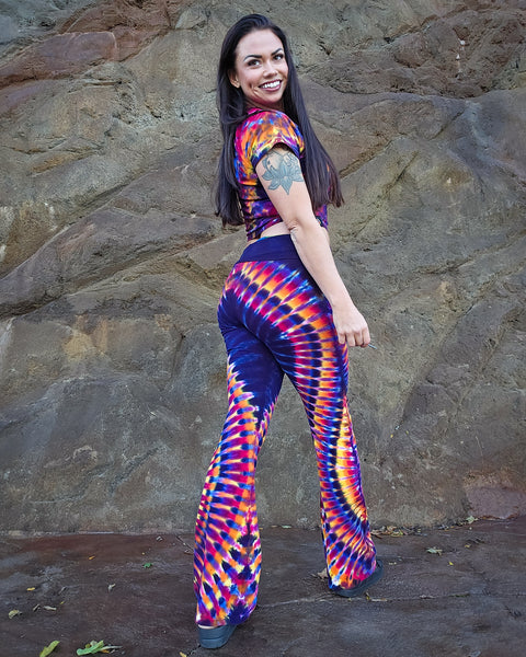 Woman wearing a colorful tie-dye outfit standing against a stone wall.