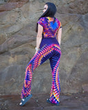 Person wearing a tie-dye outfit standing against a stone wall.
