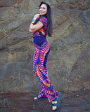 Woman wearing a colorful tie-dye outfit standing against a stone wall.
